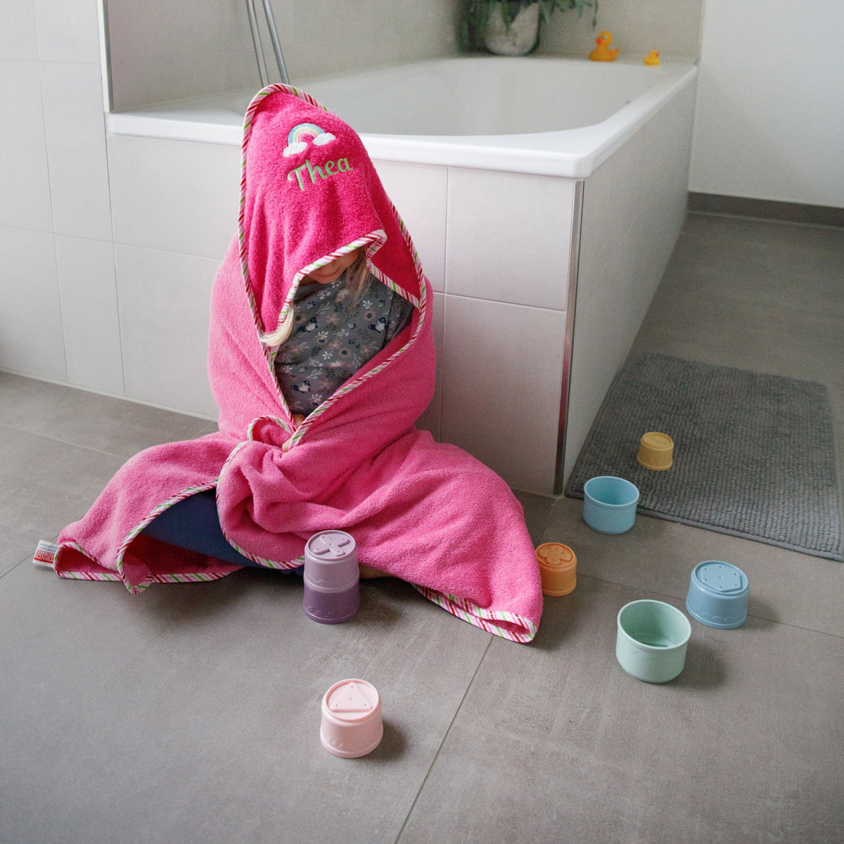 Kind spielt nach dem Baden auf Badezimmerboden im Handtuch