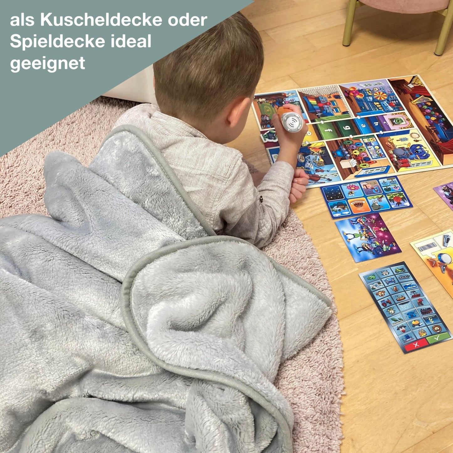 Junge liegt auf Boden und spielt und ist mit einer Kuscheldecke mit Namen zugedeckt