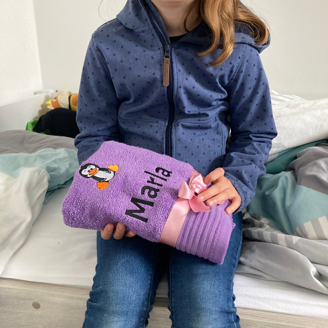 Mädchen mit besticktem Handtuch mit Namen und Motiv von Wolimbo sitzt auf Bett