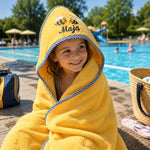 Mädchen im gelben Kapuzenhandtuch mit Bienenmotiv nach dem Schwimmen im Freibad