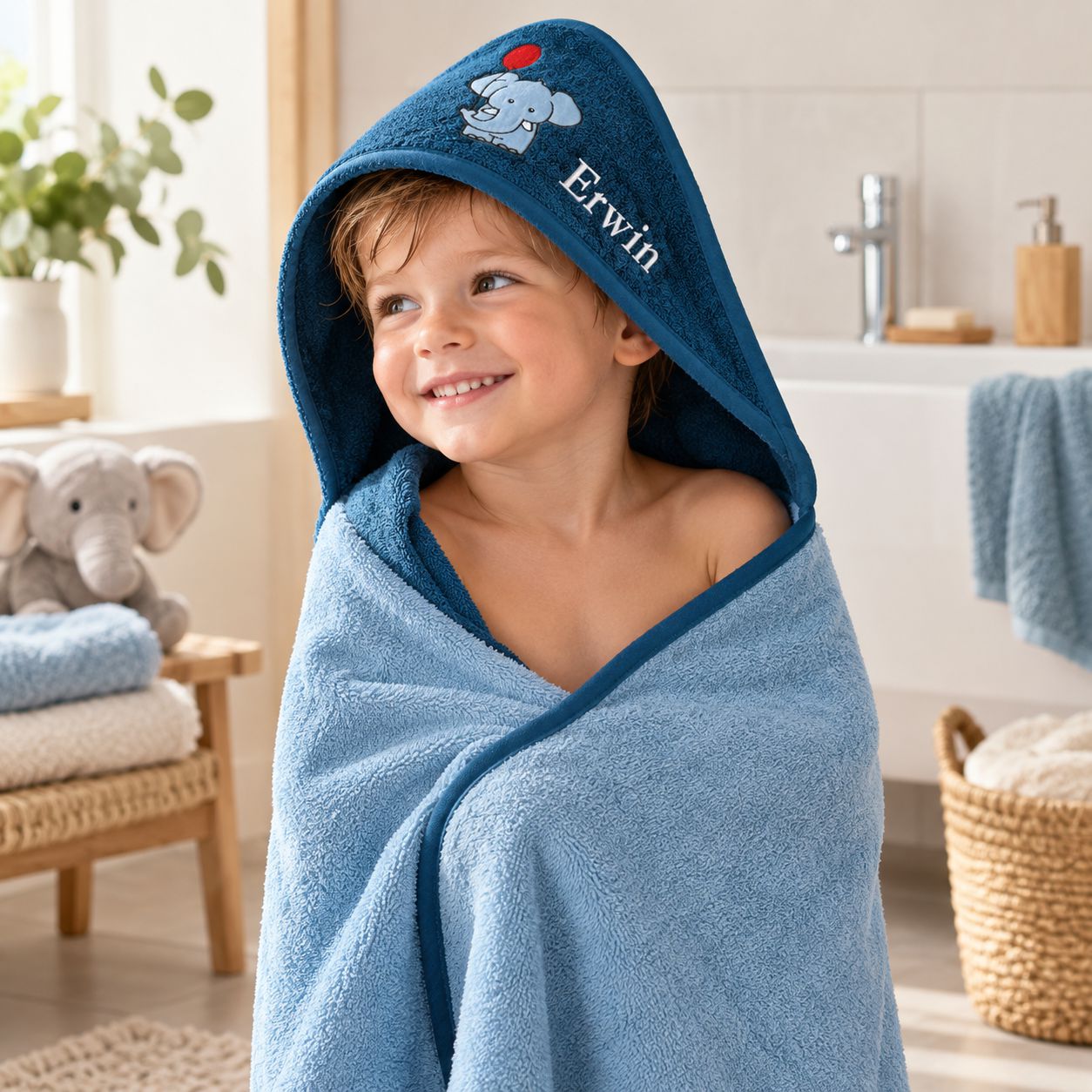 Kind mit dunkelblauem Kapuzenhandtuch, Elefantenmotiv und Namen im Badezimmer