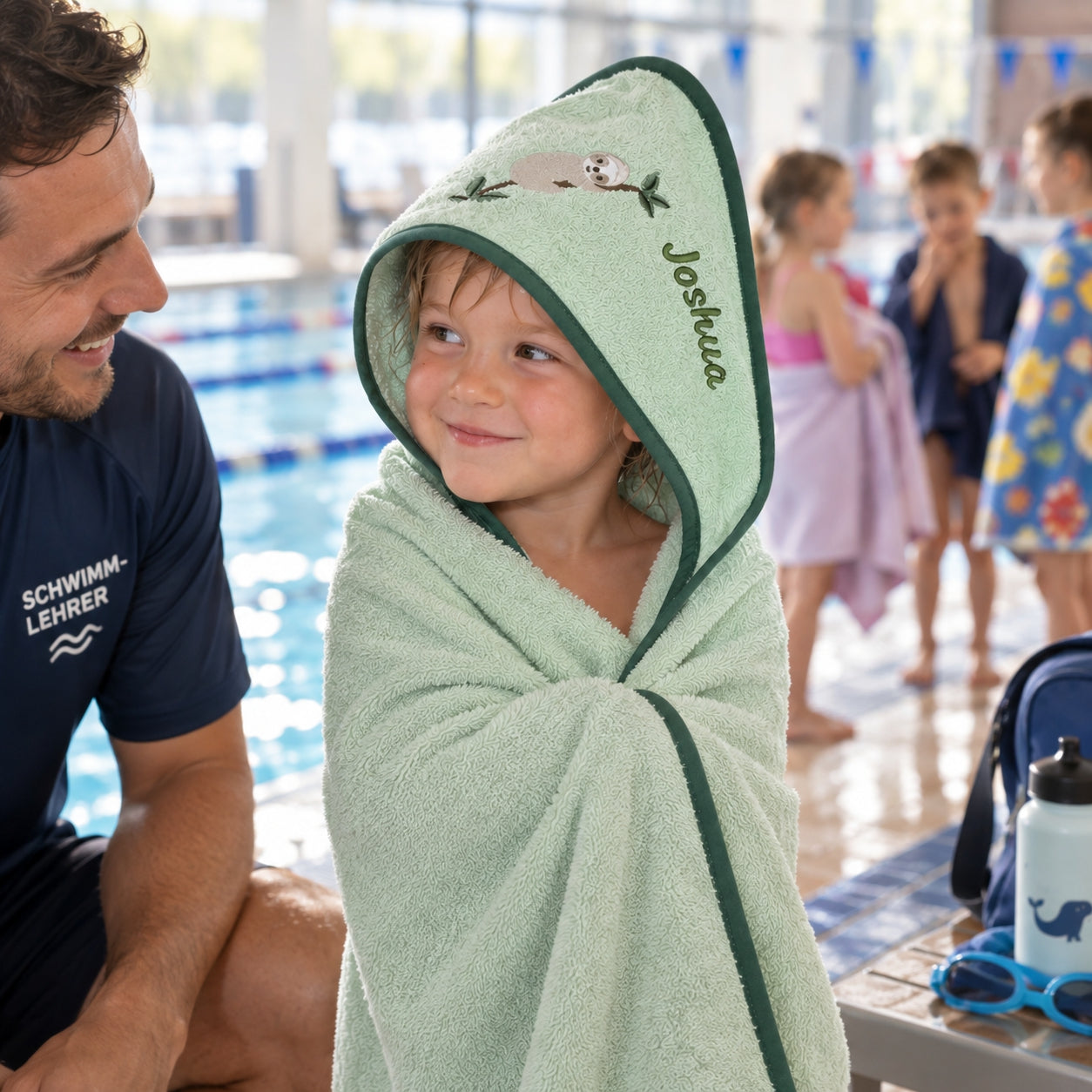 Kind im hellgrünen Kapuzenhandtuch mit Namen und Faultiermotiv im Schwimmbad