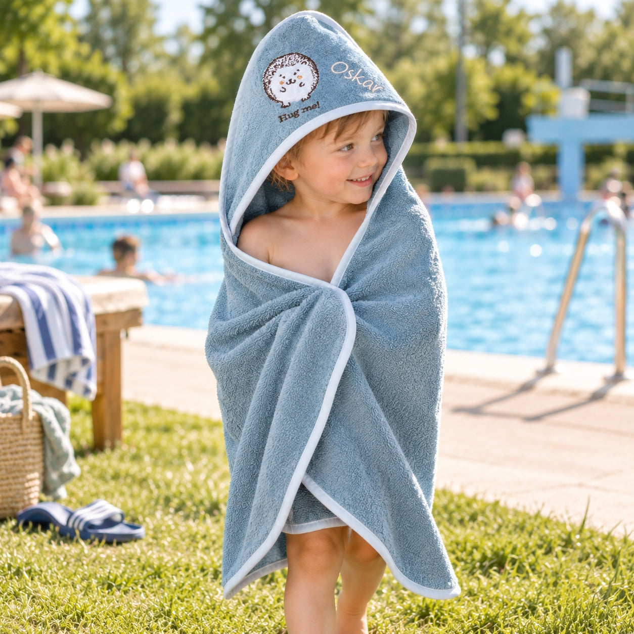 Kind im blauen Kapuzenhandtuch mit Igelmotiv am Freibad