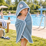 Kind im blauen Kapuzenhandtuch mit Igelmotiv am Freibad
