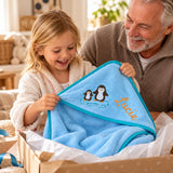 Kind und Großvater beim Auspacken des blauen Kapuzenhandtuchs mit Pinguinmotiv und Namen Lucie