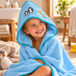 Kind mit blauem Kapuzenhandtuch, Pinguinmotiv und gesticktem Namen Lucie nach dem Baden