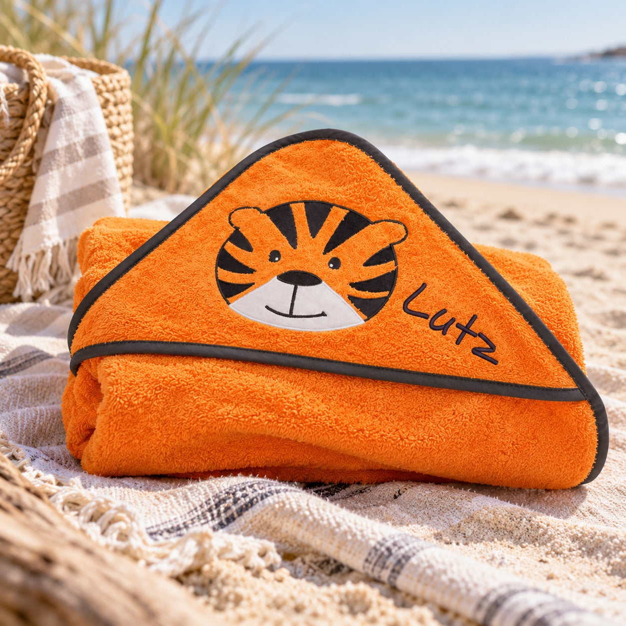 Orangefarbenes Kapuzenhandtuch mit Tigermotiv und gesticktem Namen Lutz am Strand