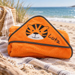 Orangefarbenes Kapuzenhandtuch mit Tigermotiv und gesticktem Namen Lutz am Strand