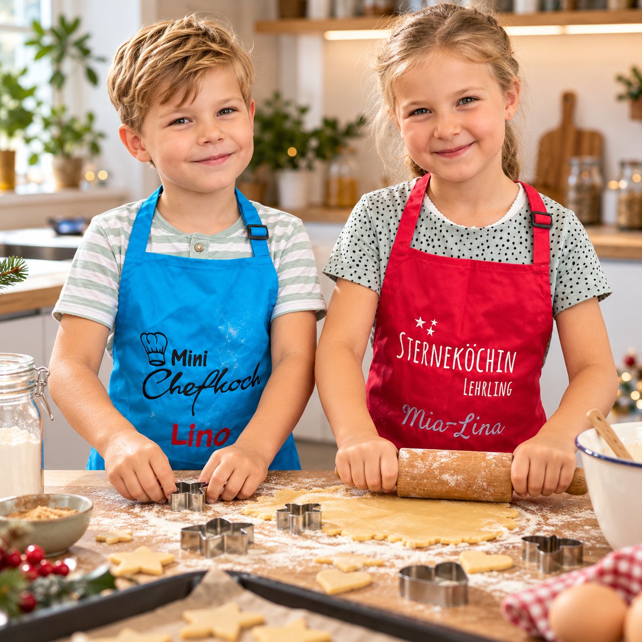 Zwei Kinder backen Plätzchen mit personalisierten Wolimbo-Kinderschürzen in Blau und Rot mit gestickten Namen.