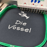Kochschürzenstoff in einer Stickmaschine mit weißer Motiv- und Schriftstickerei