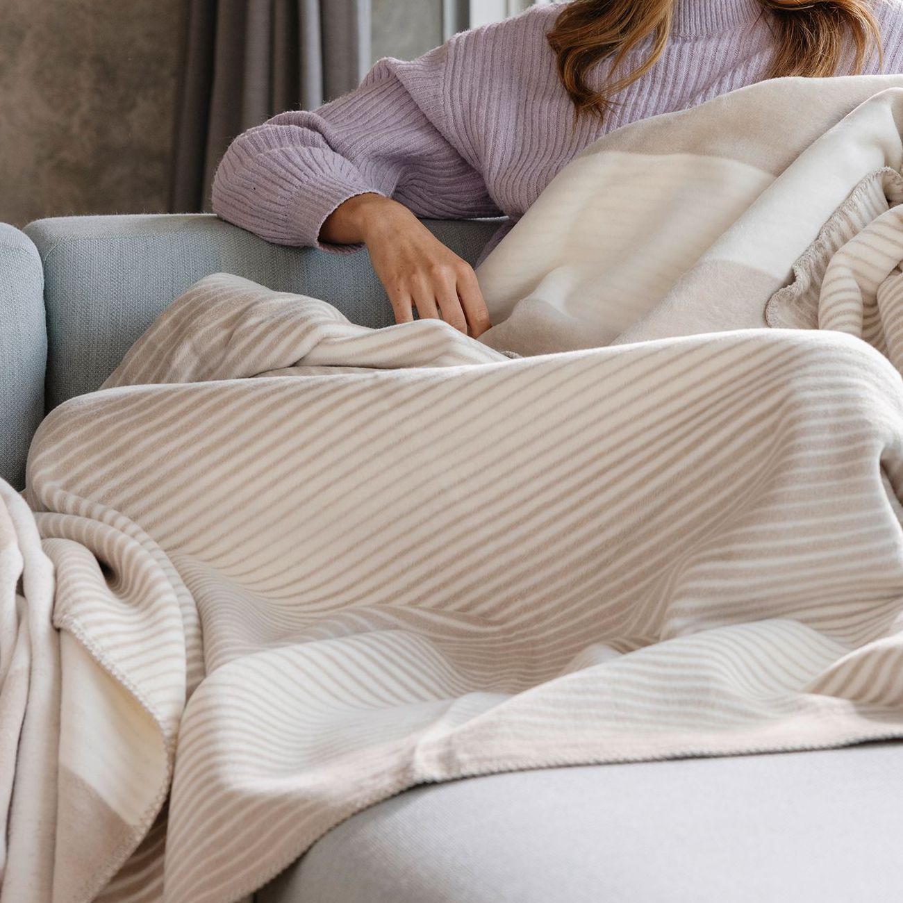 Frau auf dem Sofa mit beige-weiß gestreifter Wohndecke