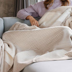 Frau auf dem Sofa mit beige-weiß gestreifter Wohndecke