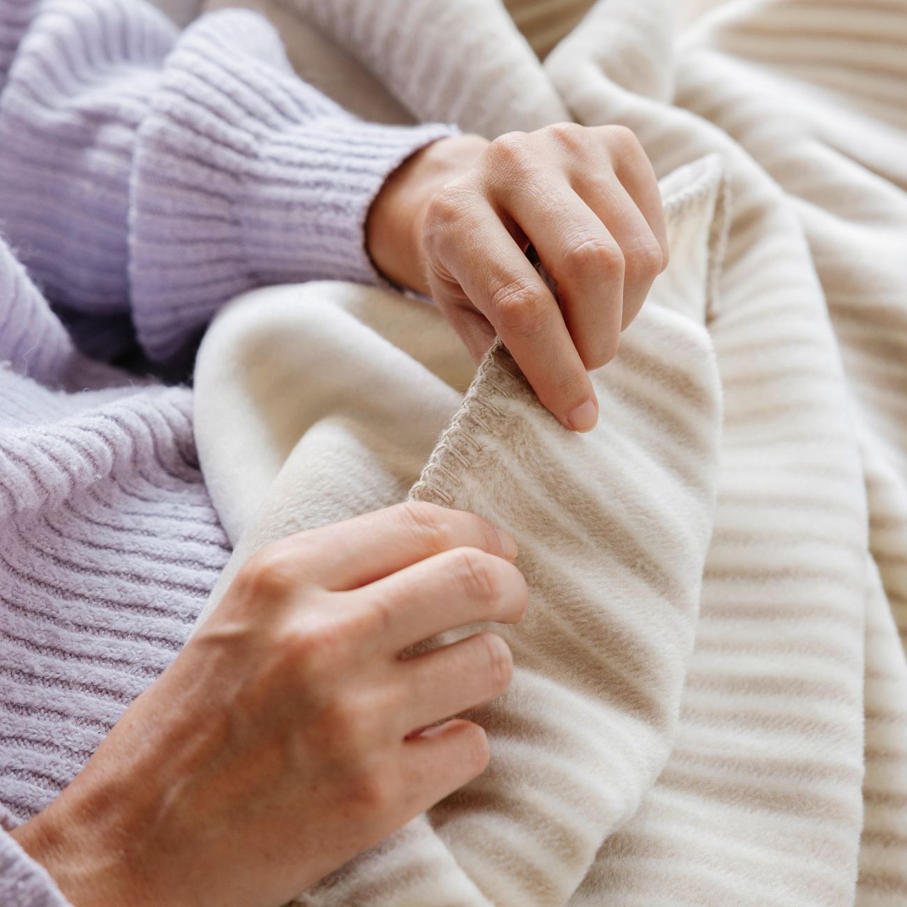 Hände zeigen die weiche Oberfläche und Kante der beige-weißen Wohndecke