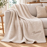 Personalisierte beige-weiße Wohndecke mit Namen auf einem hellen Sofa