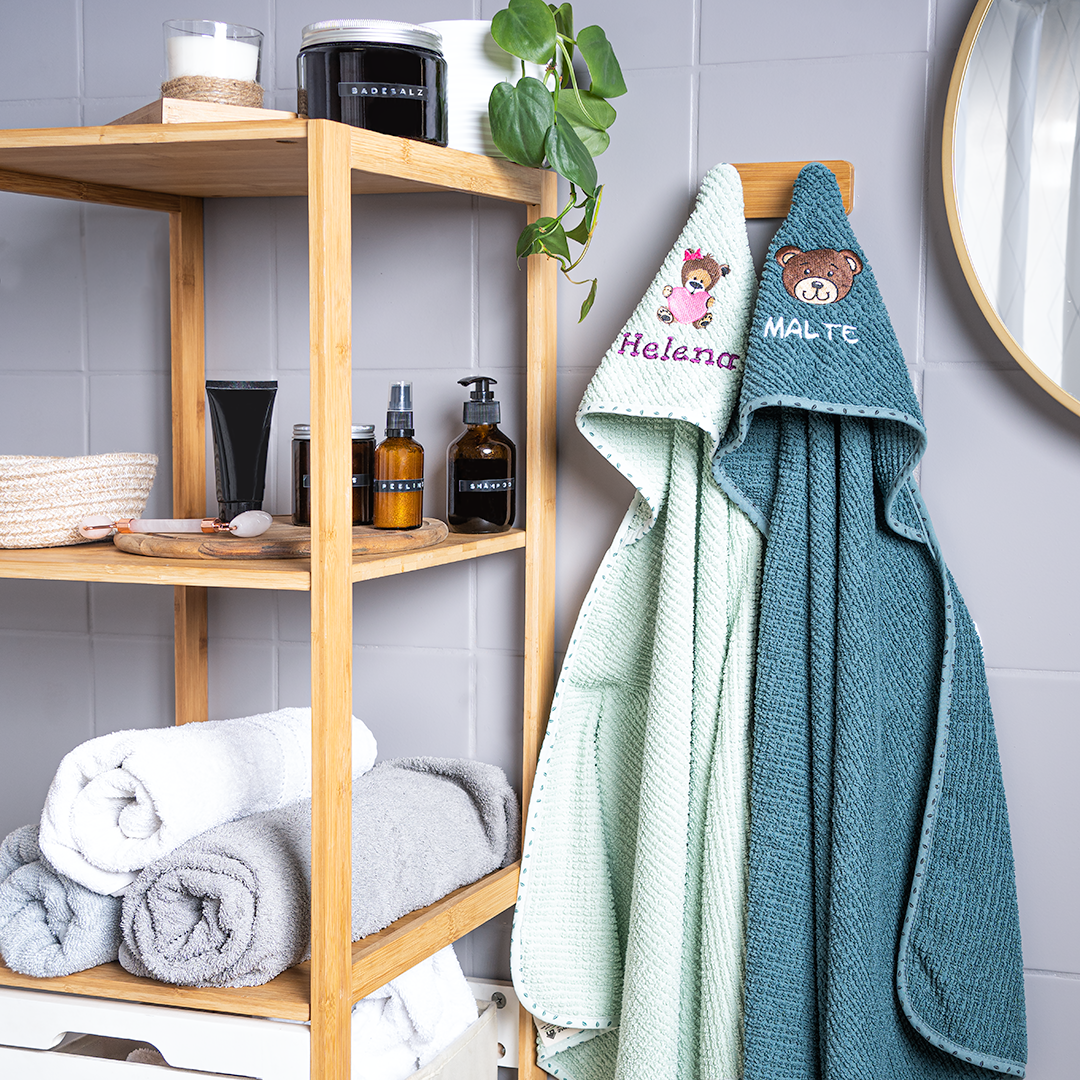 Kapuzenhandtücher hängen an Haken im Badezimmer - mit Namen bestickt und Motiv