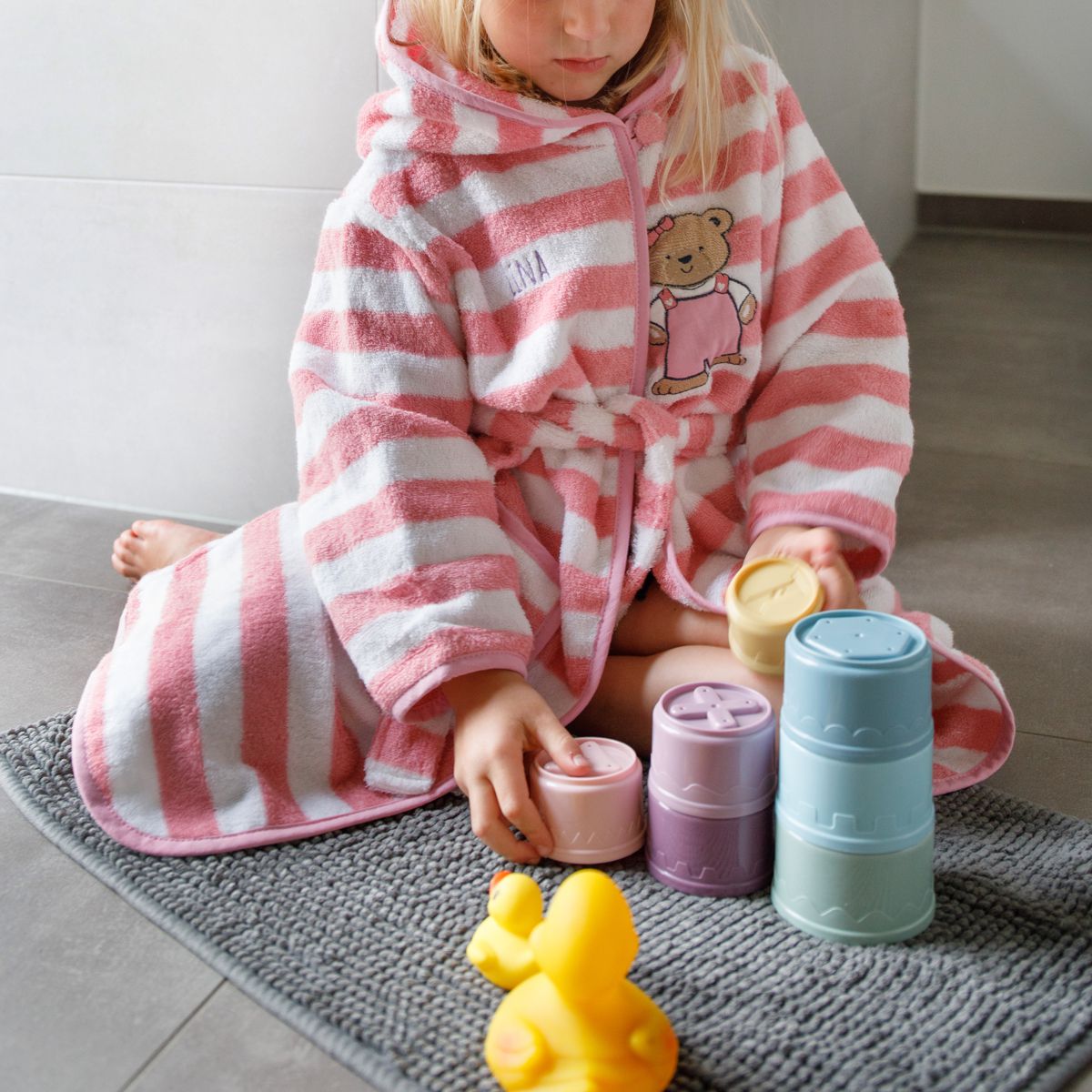 Mädchen sitzt auf Teppich mit Bademantel